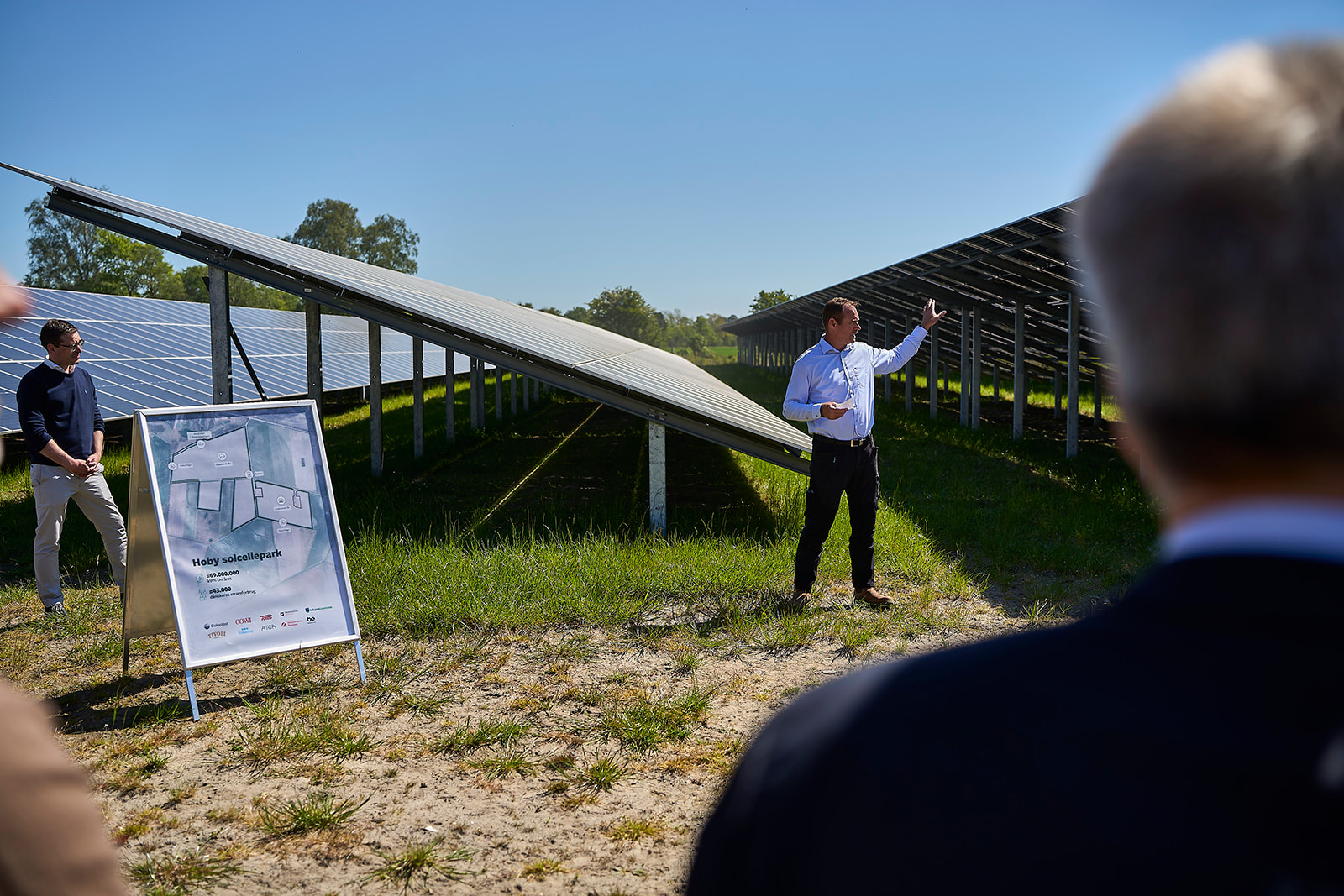 Image of a man pointing to solar panels behind him